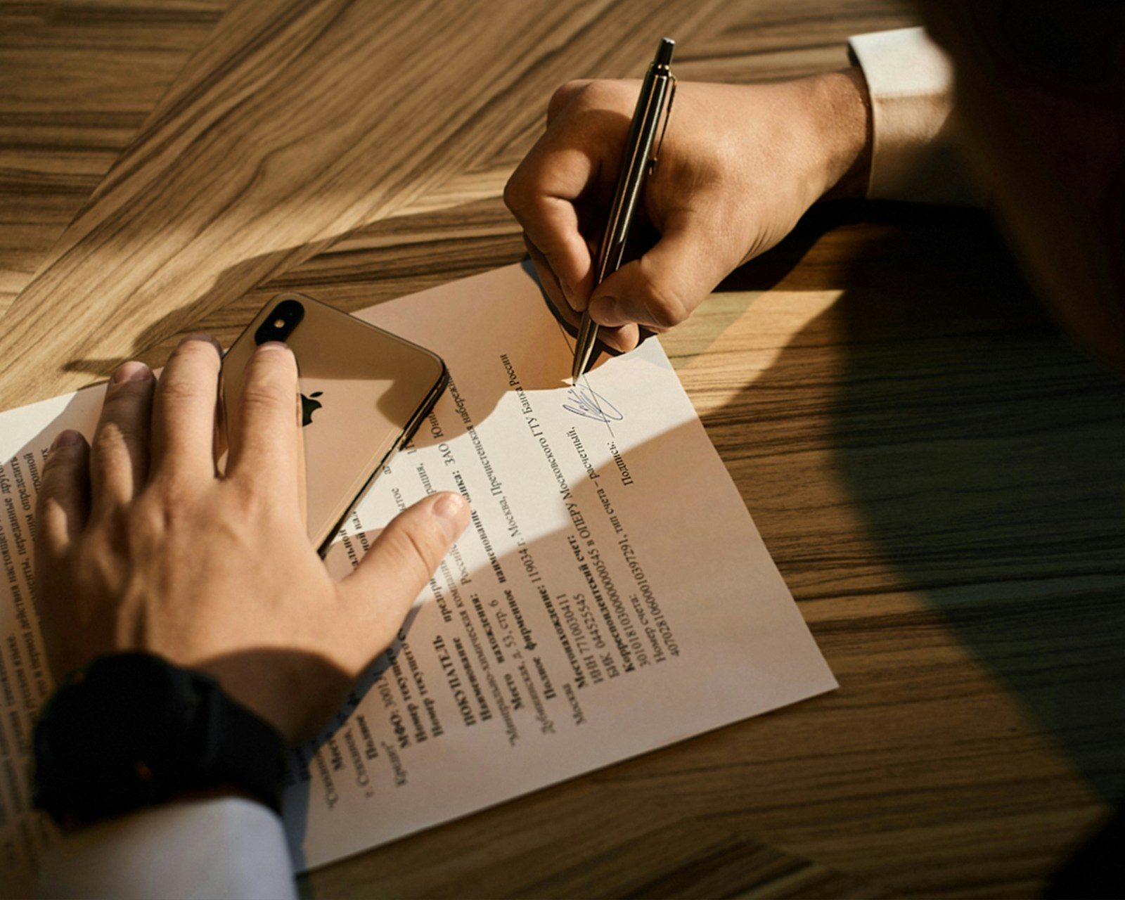 Hand die met een pen een document ondertekent op een houten tafel