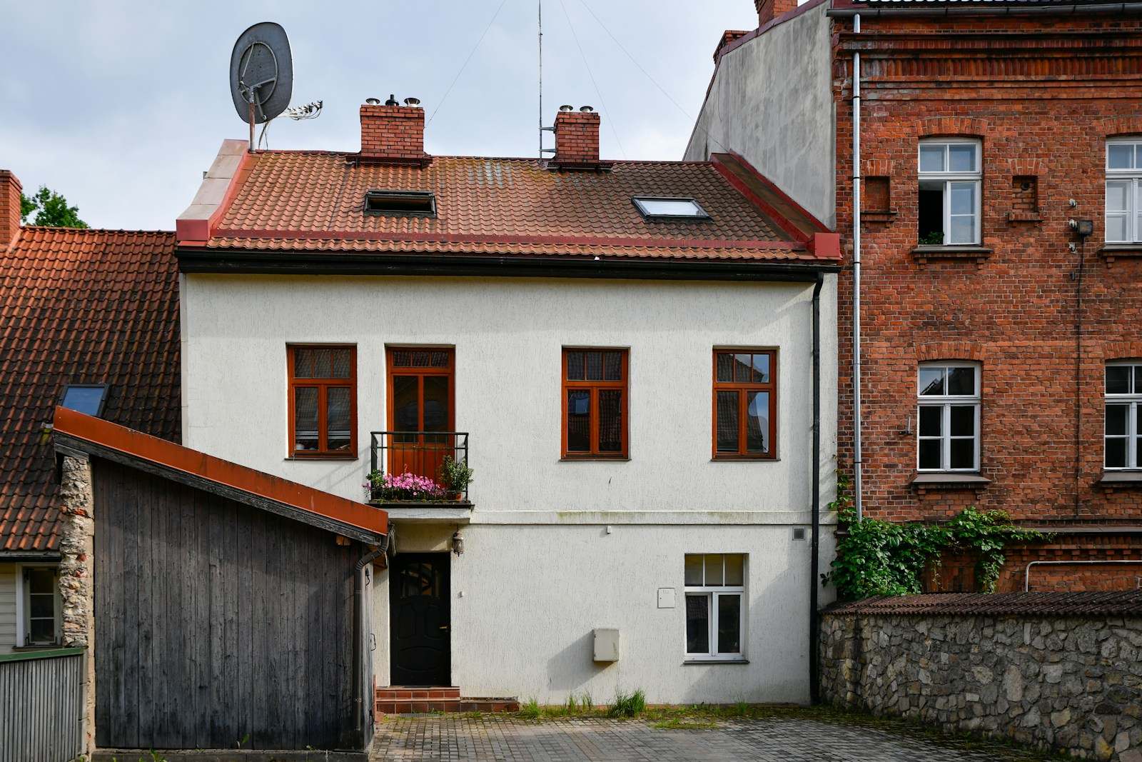 Wit bepleisterde woning met rode dakpannen tussen bakstenen gebouwen