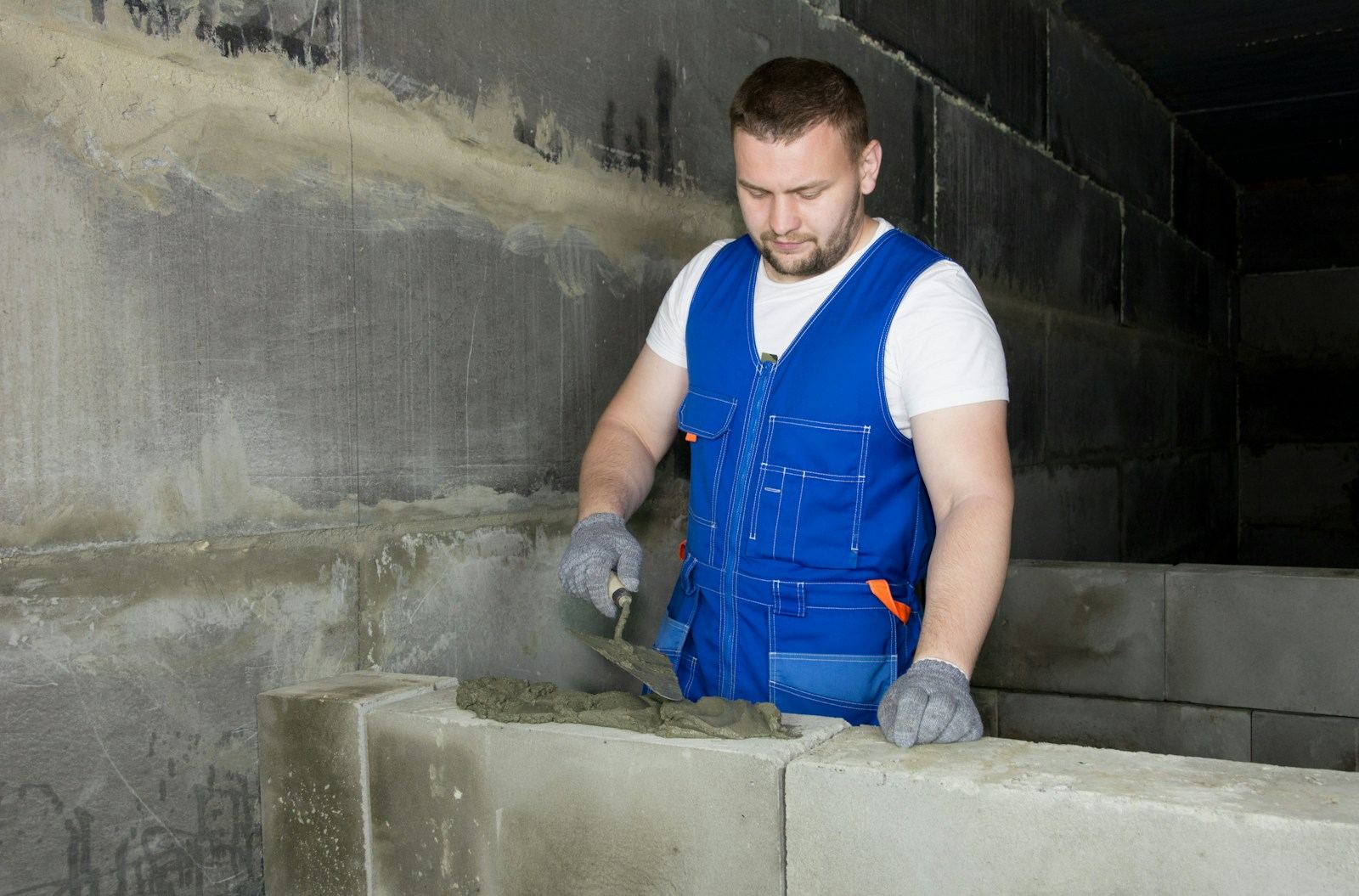 Vakman in een blauwe overall die met een troffel mortel op een rij betonblokken aanbrengt